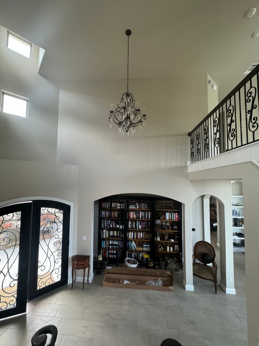 Spacious living room with chandelier, black double doors, and towering bookshelves.