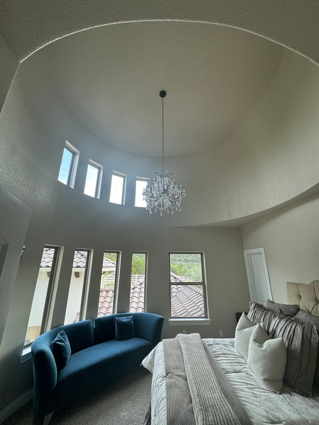 Modern bedroom with a curved ceiling, chandelier, blue couch, and large windows for natural light.