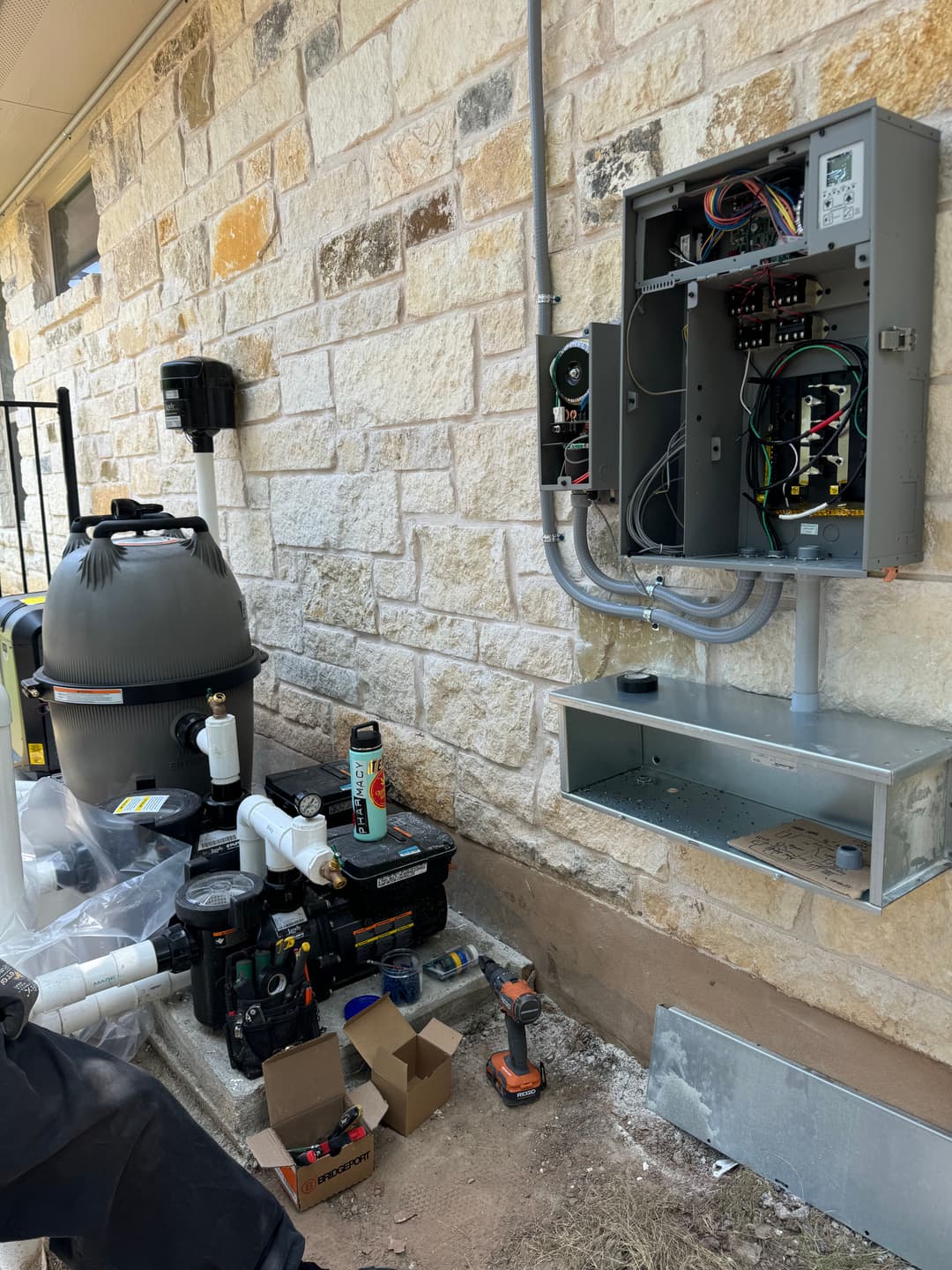 Pool equipment setup with control panel and filtration system installed on stone wall.