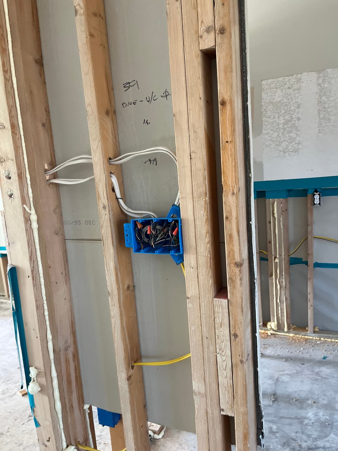 Electrical wiring installation between wooden studs in a drywall construction site.