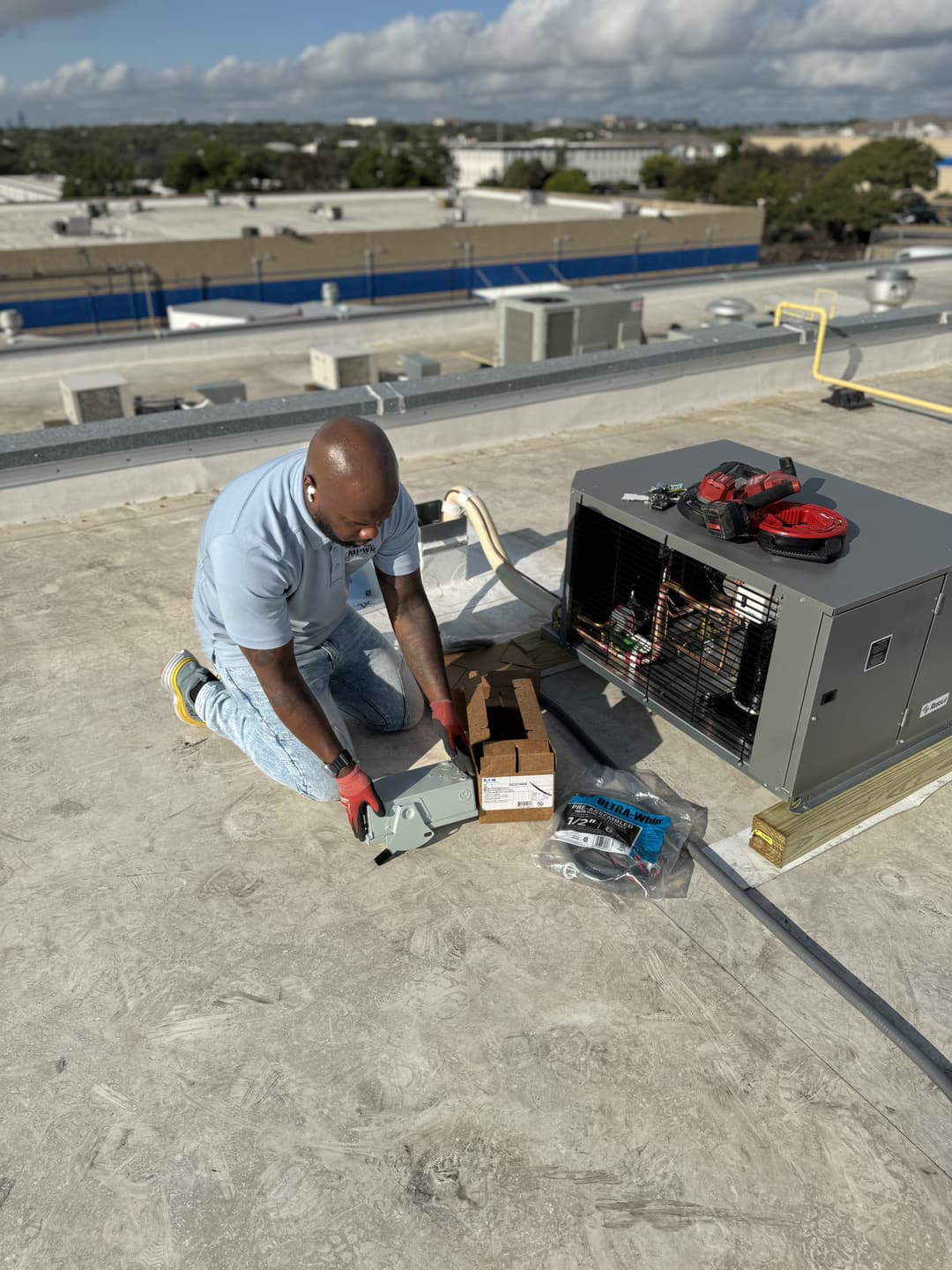 Technician installing HVAC unit on rooftop with tools and parts nearby.