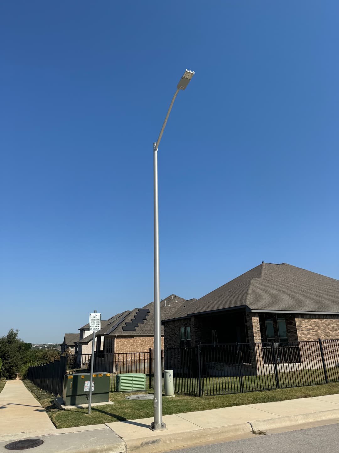 Streetlight next to a sidewalk in a residential area with houses and clear blue sky.