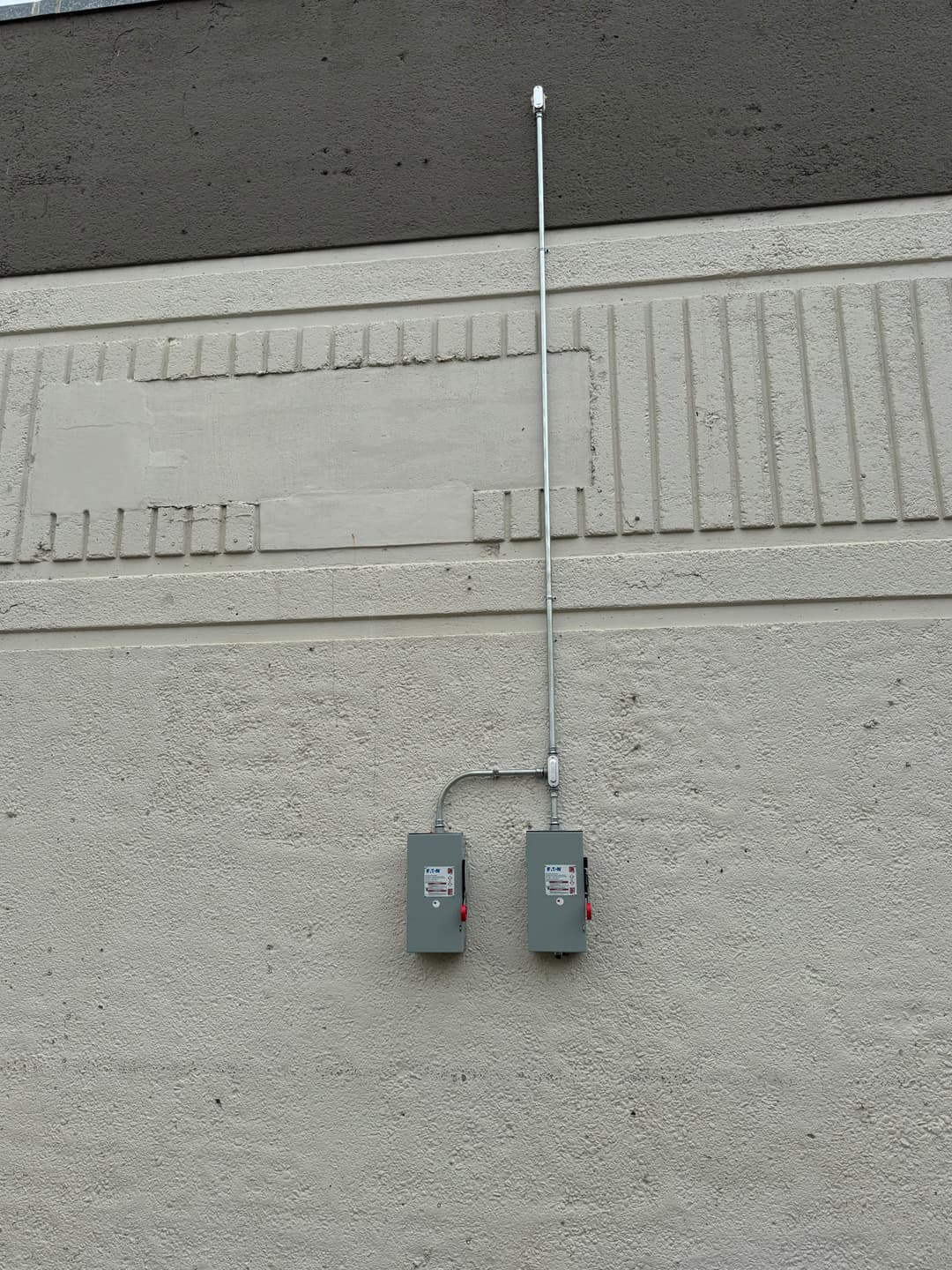Electrical boxes mounted on a textured wall with vertical conduit pipe.