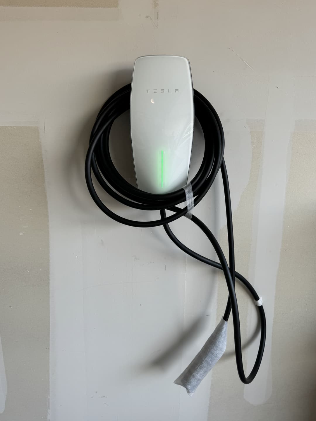 Tesla wall-mounted EV charger with charging cable, green light indicating readiness.