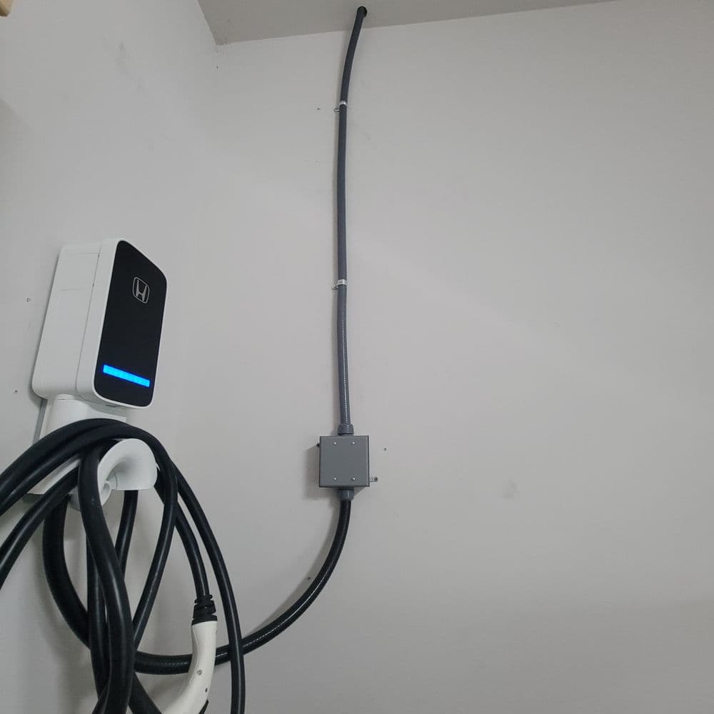 Wall-mounted electric vehicle charger with cable, connected to a junction box.