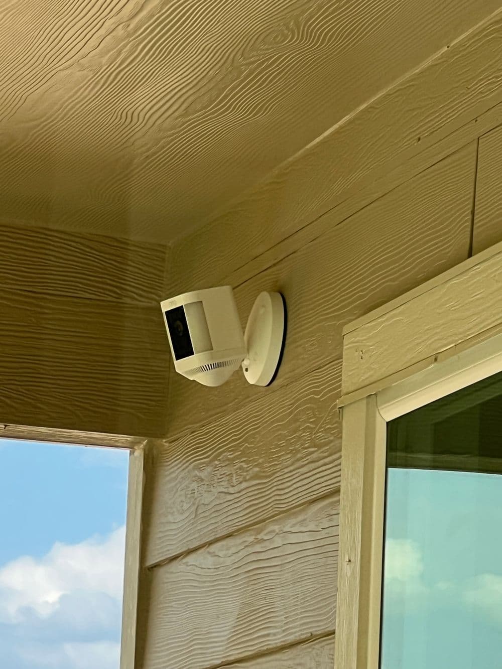 Outdoor security camera mounted on a house wall with a view of the sky.