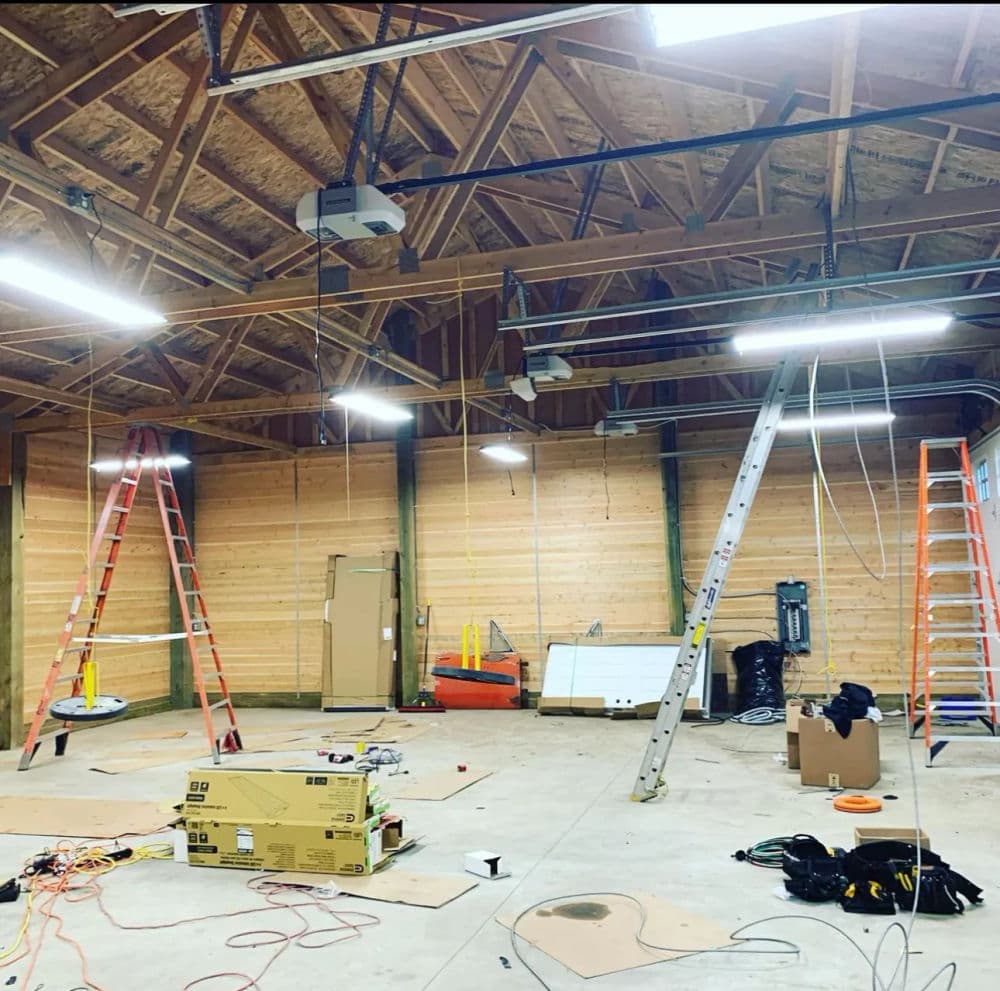 Interior of a work area with ladders, lighting fixtures, and electrical wiring in progress.