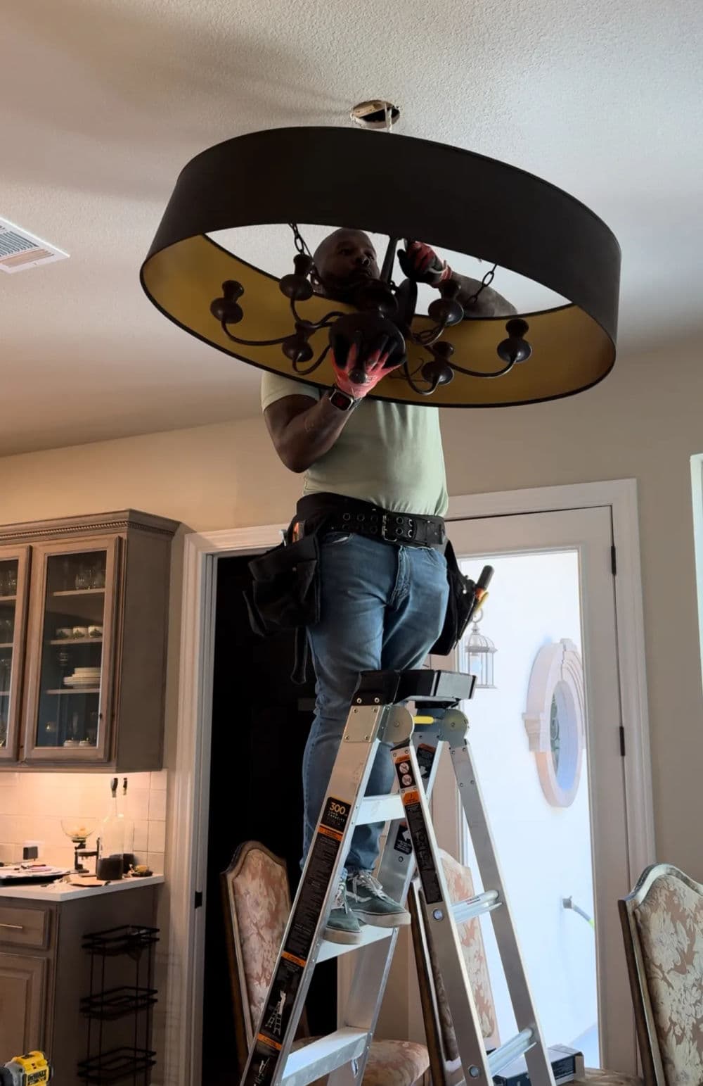 Person on ladder installing chandelier in a modern kitchen.