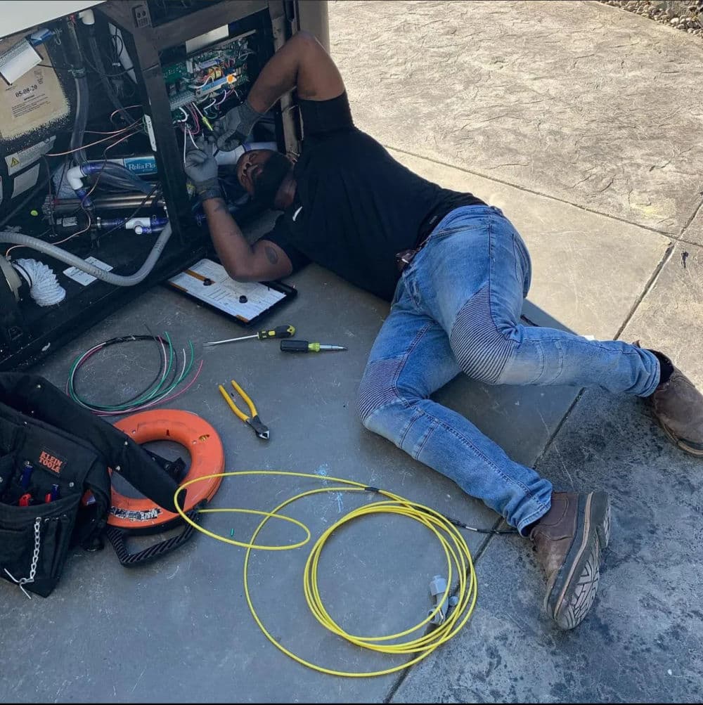 Technician repairing equipment, laying on ground with tools and wires scattered around.