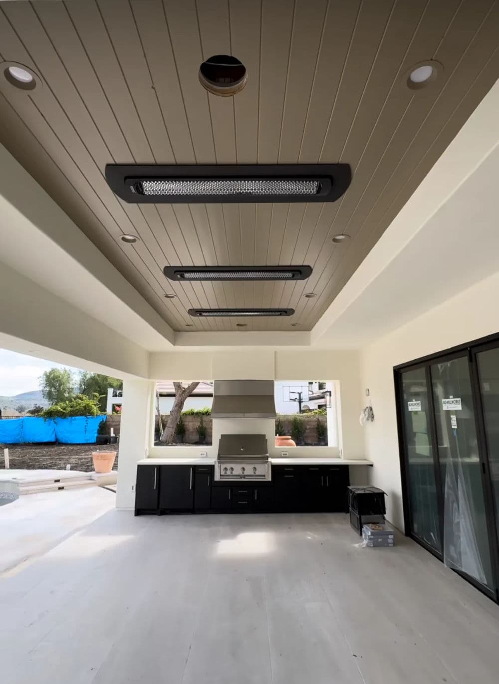 Modern outdoor kitchen with sleek design, stainless steel appliances, and ceiling heaters.
